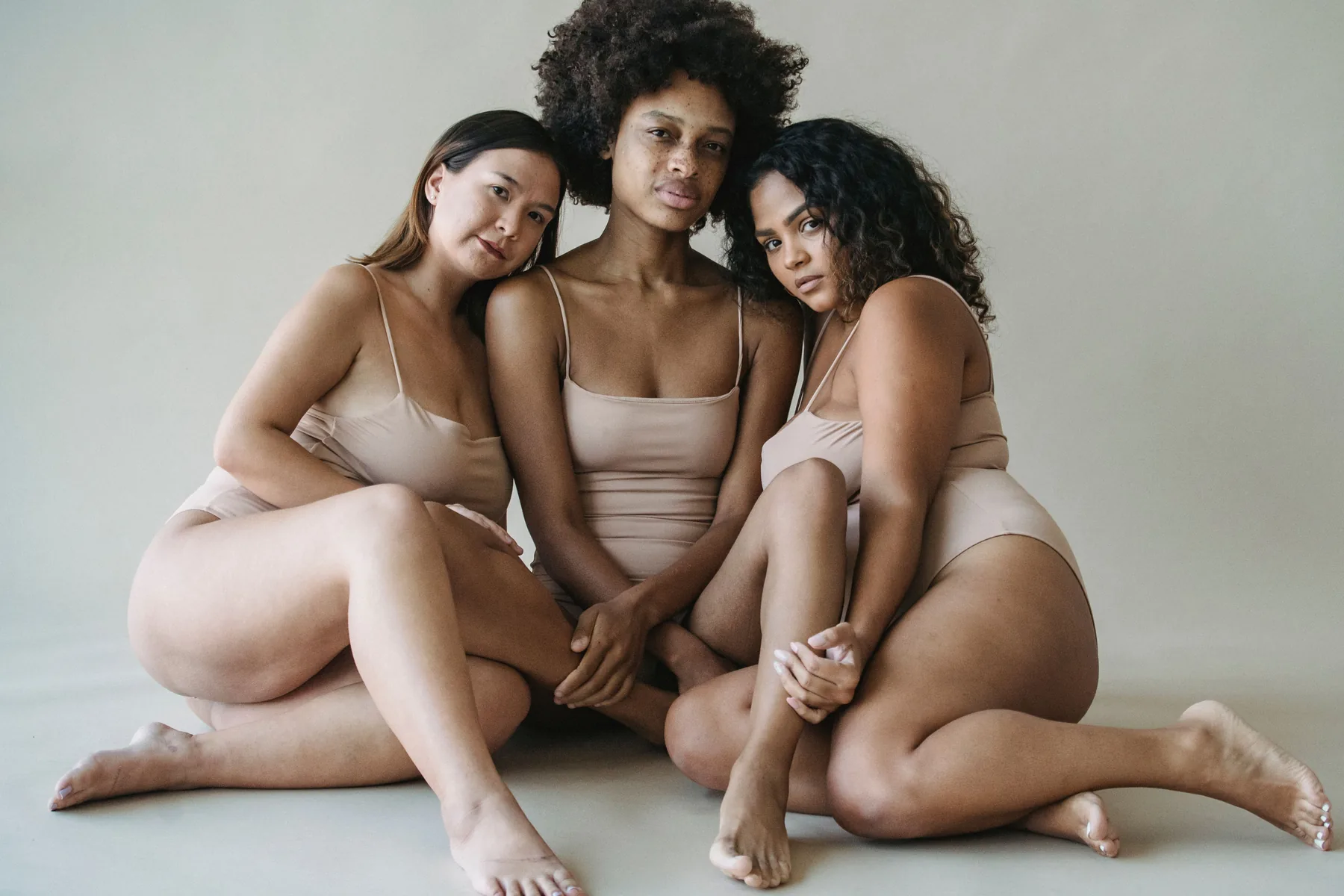 Three women wearing neutral-toned bodysuits